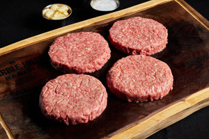 Four hamburger patties arranged on a wooden cutting board, ready for grilling and assembling into burgers.