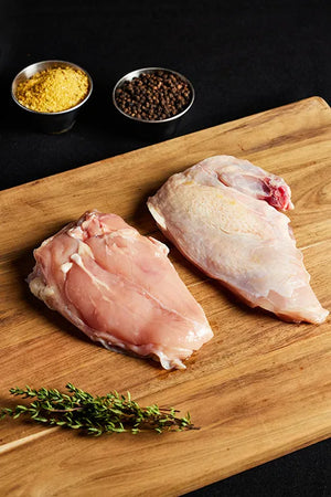 Two raw airline chicken breasts on a cutting board, surrounded by various spices.