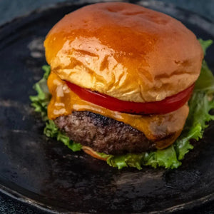 A Black Angus burger with cheese and tomato served on a sleek black plate.