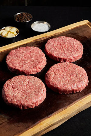 Four Black Angus burger patties arranged on a wooden cutting board, ready for grilling or preparation.