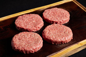 Four fresh Black Angus burger patties placed on a cutting board.