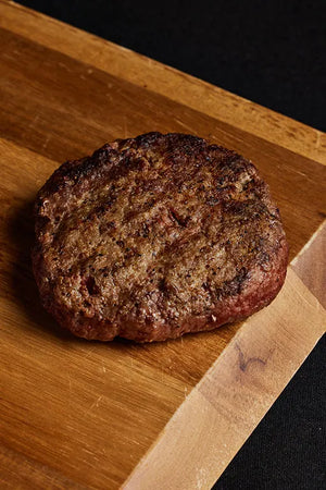 A Black Angus burger patty on a wooden cutting board, showcasing its texture and appearance.