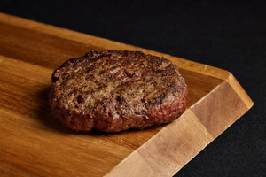 A grilled Black Angus burger placed on a wooden cutting board.