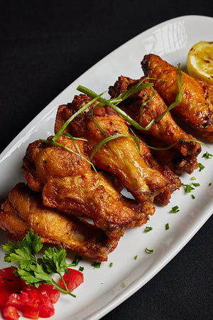 A serving of cooked chicken wings accompanied by lemon wedges and fresh garnish.