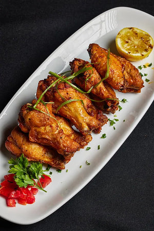 A serving of cooked chicken wings accompanied by lemon wedges and fresh garnish.