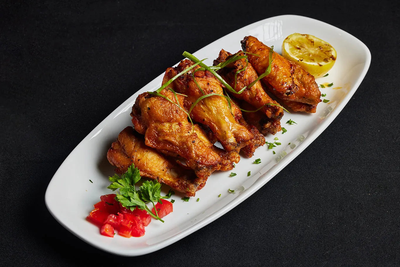 A serving of grilled chicken wings accompanied by lemon wedges and fresh garnish.