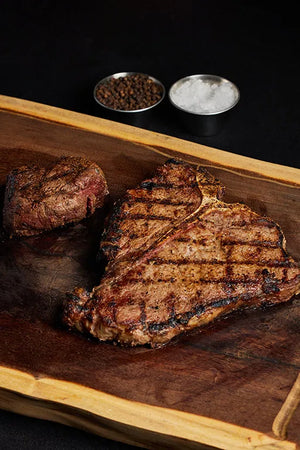 A T-Bone and Filet Mignon steak on a wooden cutting board, ready to be prepared with spices.