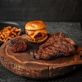 A T-Bone steak, Filet Mignon and a burger displayed on a wooden board, showcasing a meat bundle.