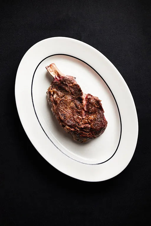 A cooked Cowboy Ribeye steak served on a white plate.