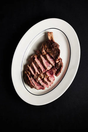 A plate featuring a Cowboy Ribeye steak, cooked and garnished, ready to be enjoyed.