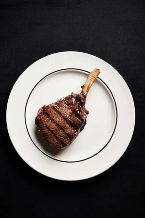 A Cowgirl Ribeye steak elegantly presented on a white plate.