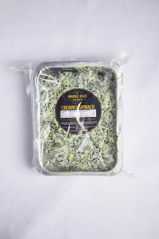 A plastic container filled with creamed spinach placed on a clean white surface.