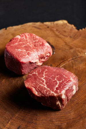 Two USDA Choice filet mignon steaks displayed on a wooden cutting board.