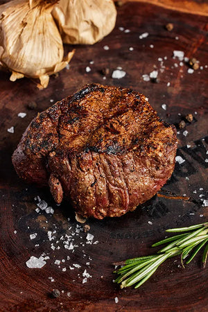 A grilled USDA Choice filet mignon steak displayed on a wooden cutting board, accompanied by garlic and rosemary.