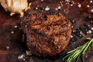 A grilled USDA Choice filet mignon steak displayed on a wooden cutting board, accompanied by garlic and rosemary.