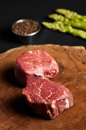 Two USDA Choice Filet Mignon steaks on a wooden cutting board, accompanied by asparagus and spices.