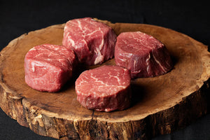 Four Filet Mignon steaks arranged on a wooden board.