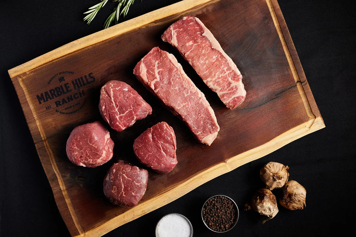 A cutting board displaying Filet Mignons and New York Strips, surrounded by an array of spices for seasoning.