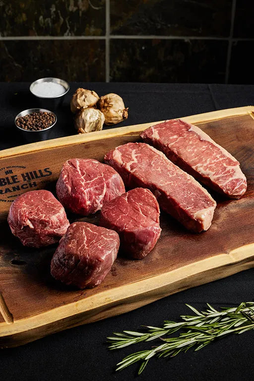 A cutting board displaying Filet Mignons and New York Strips, surrounded by an array of spices for seasoning.