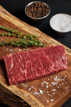 A top sirloin steak resting on a cutting board, garnished with salt and pepper for seasoning.