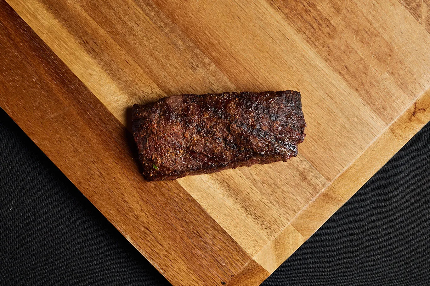 A grilled flatiron steak placed on a wooden cutting board.