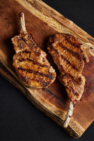 Two grilled pork chops resting on a rustic wooden cutting board.