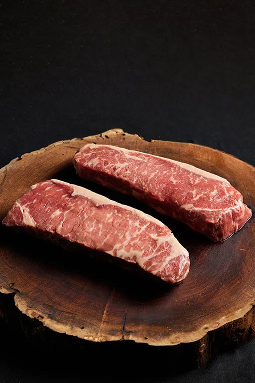 A wooden board displays two USDA Prime New York Strip steaks.