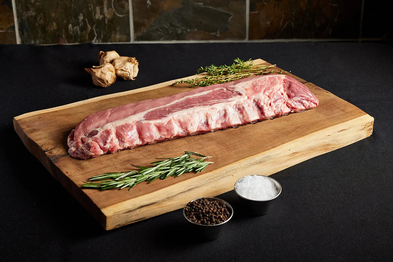 A rack of pork baby back ribs displayed on a wooden cutting board, ready for cooking with herbs and garlic.