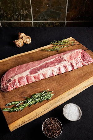 A rack of pork baby back ribs displayed on a wooden cutting board, ready for cooking with herbs and garlic