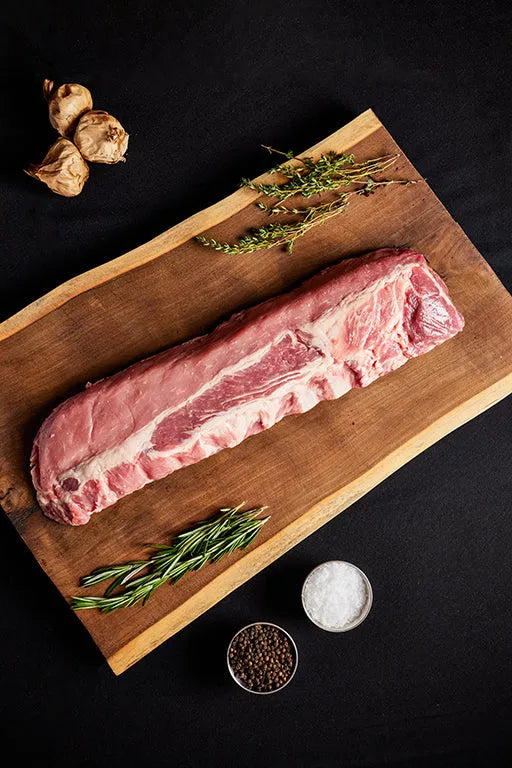 A rack of pork baby back ribs displayed on a wooden cutting board, ready for cooking with herbs and garlic.