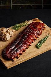 A rack of pork baby back ribs displayed on a wooden cutting board, ready for serving and complemented with herbs and garlic