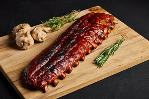 A rack of pork baby back ribs displayed on a wooden cutting board, ready for serving and complemented with herbs and garlic