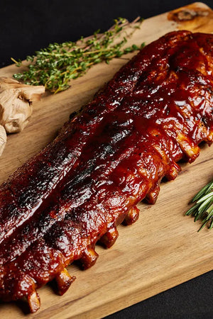 A rack of pork baby back ribs displayed on a wooden cutting board, ready for serving and complemented with herbs and garlic.