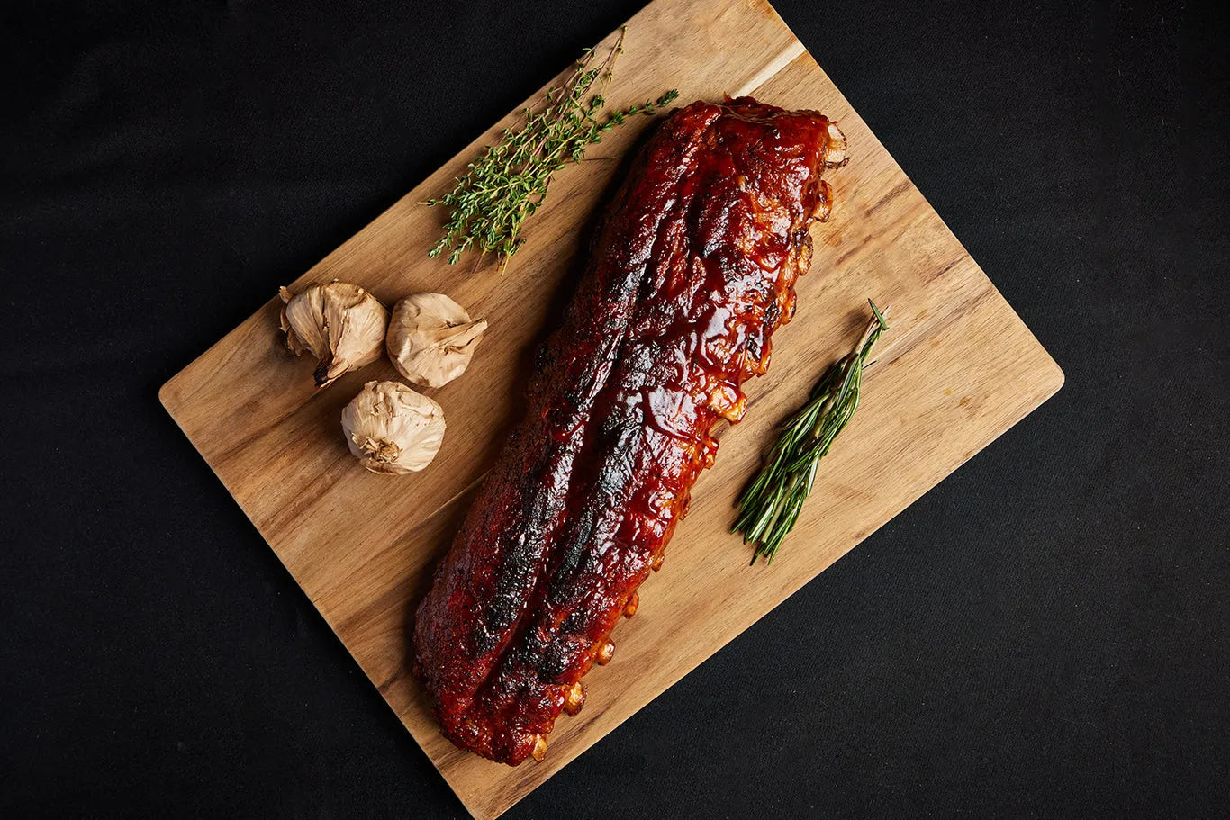 A rack of pork baby back ribs displayed on a wooden cutting board, ready for serving and complemented with herbs and garlic.