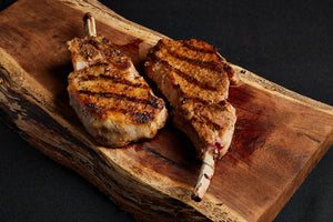 Two grilled pork chops resting on a rustic wooden cutting board.