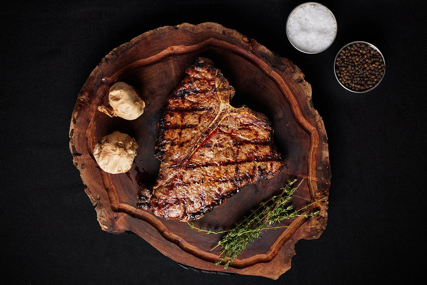 A grilled Porterhouse USDA Choice steak rests on a wooden cutting board, surrounded by herbs and spices.