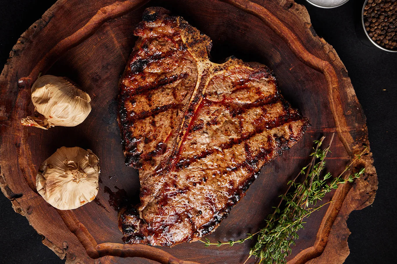 A grilled Porterhouse USDA Choice steak rests on a wooden cutting board, surrounded by herbs and spices.