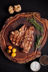 A grilled Porterhouse USDA Choice steak rests on a wooden cutting board, surrounded by herbs and spices.