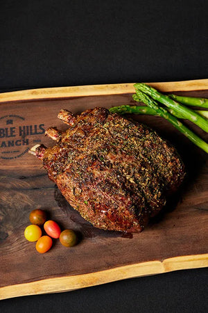 A succulent 3-bone prime rib roast on a cutting board, accompanied by fresh asparagus and ripe tomatoes.