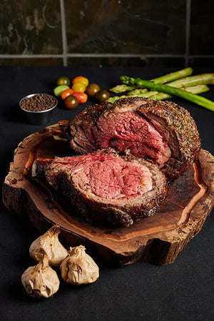 A 3-bone prime rib roast steak displayed on a wooden board, accompanied by a variety of fresh vegetables.