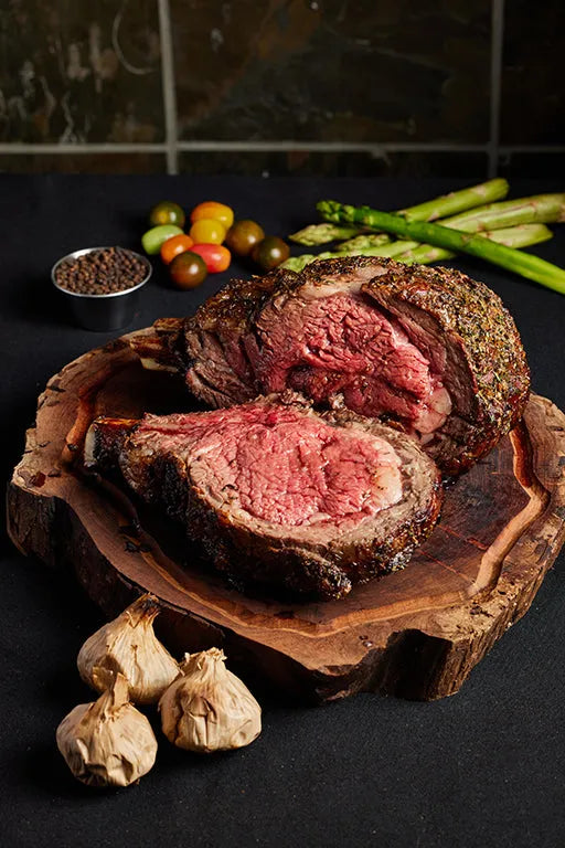 A 3-bone prime rib roast steak displayed on a wooden board, accompanied by a variety of fresh vegetables.