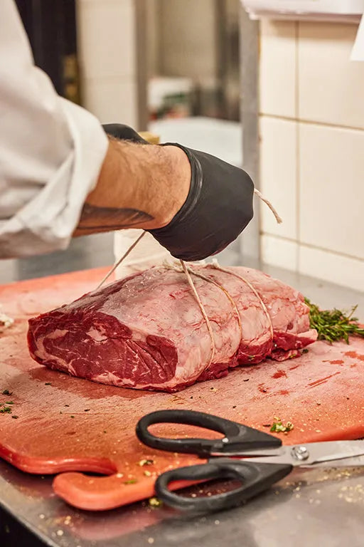 A chef preparing a boneless prime rib roast to be sliced on a wooden cutting board.