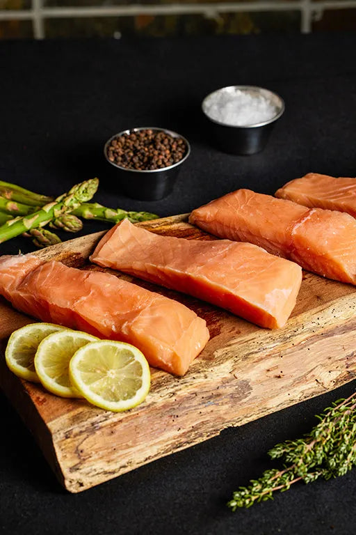 Fresh salmon fillets arranged on a wooden cutting board, garnished with lemon slices and asparagus.