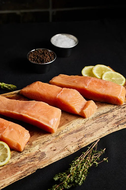 Fresh salmon fillets arranged on a wooden cutting board, garnished with lemon slices and asparagus.