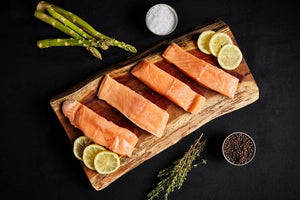 Fresh salmon fillets arranged on a wooden cutting board, garnished with lemon slices and asparagus.