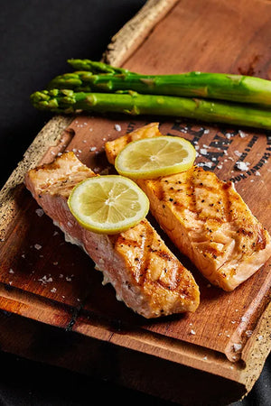 Grilled salmon filet and asparagus arranged on a rustic wooden cutting board.