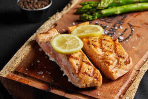 Grilled salmon filet and asparagus arranged on a rustic wooden cutting board.