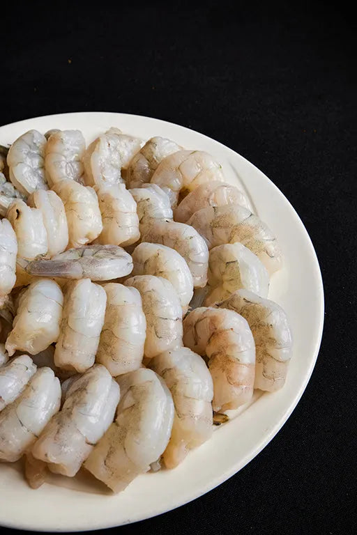 A white plate of fresh shrimp arranged on a black background.