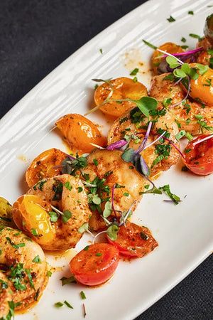 A white plate of shrimp and tomatoes arranged and ready to eat.