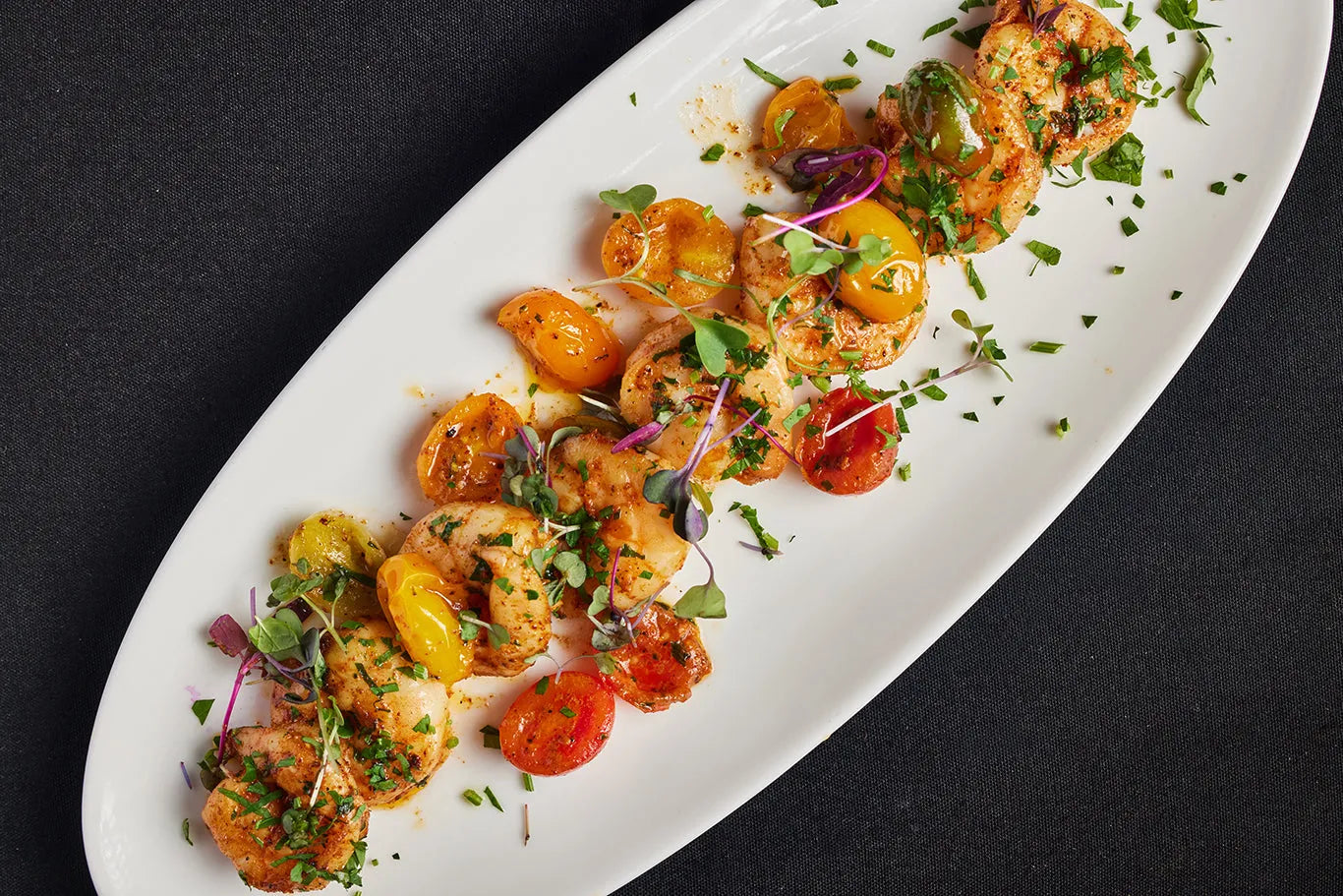 A white plate of shrimp and tomatoes arranged and ready to eat.